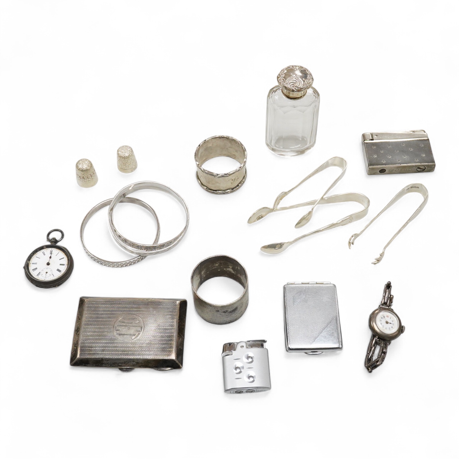 A collection of small silver to include a cigarette case, two napkin rings, three pairs of sugar tongs, a thimble, a lady's wrist watch and a mounted glass toilet jar. together with a 925 fob watch, a 935 mounted lighter